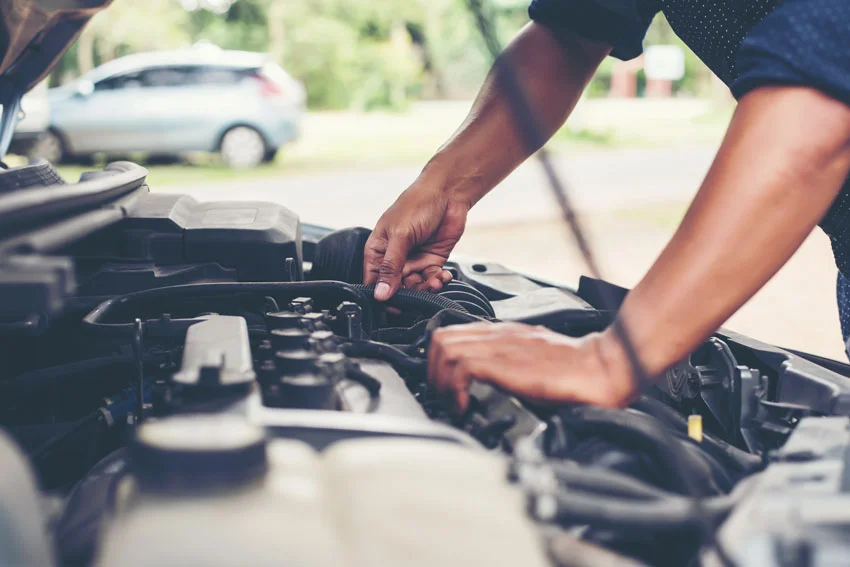 A service image of an auto technician standing over the exposed hood of a vehicle