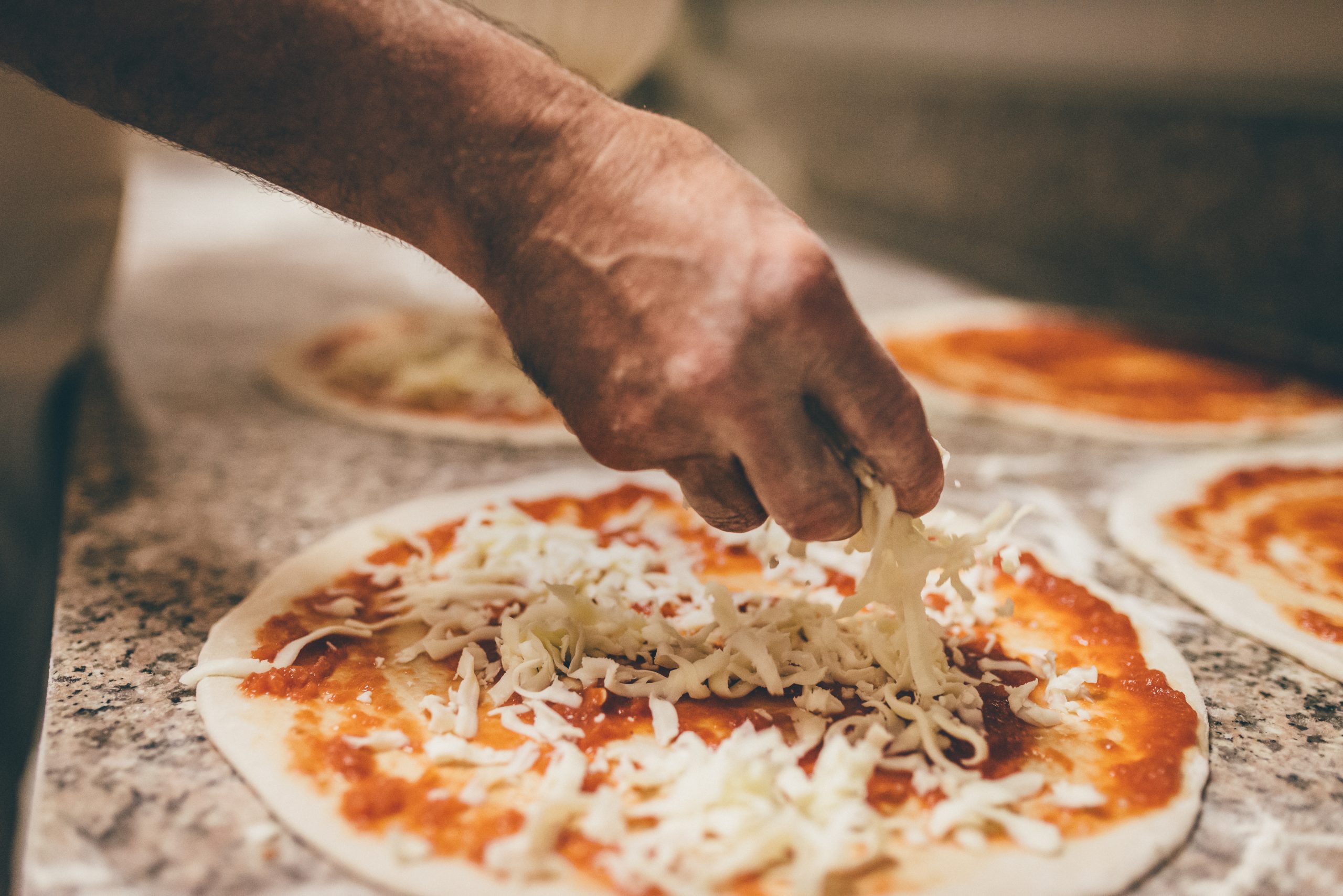 The hands of a chef sprinkling mozzarella cheese on a pizza