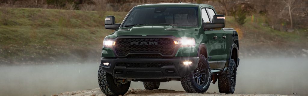 The image showcases a rugged green RAM 1500 Rebel truck, standing out with its bold and adventurous look, designed for off-road experiences, captured in a natural outdoor setting.
