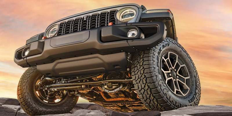 Low-angle front view of a Jeep Gladiator on rocks at sunset.